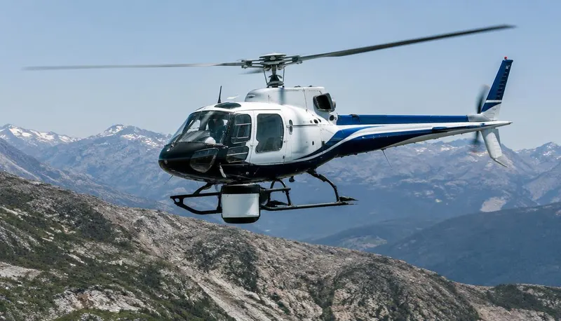 Survey helicopter with a sensor pod flying over mountain terrain