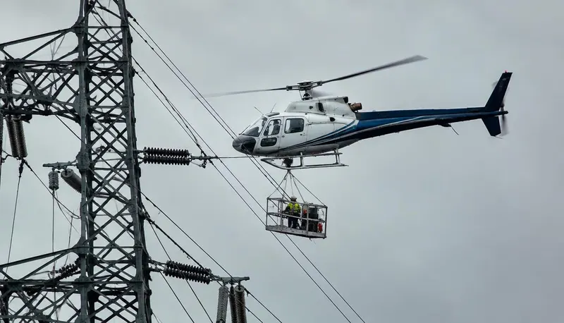 Helicopter working alongside a high-voltage transmission tower