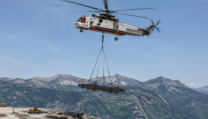 Helicopter carrying a sling load above a mountain construction site